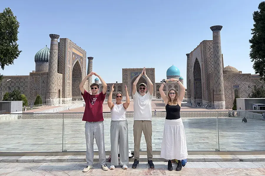 Four people pose with arms raised to form O-H-I-O in front of an ornate historic plaza with blue domes and tiled buildings.
