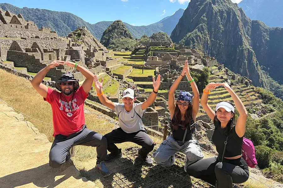 Four people pose with raised arms spelling O-H-I-O in front of the ruins of Machu Picchu and surrounding mountains.
