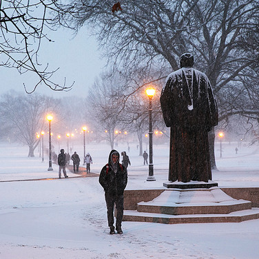 Lampposts on the Oval cast a warm glow over a snowy scene for students on their way to class or study sessions at the library.