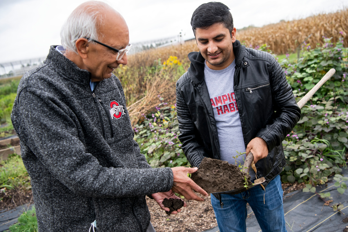 Rattan Lal and a fellow researcher look at a shovelful of soil.