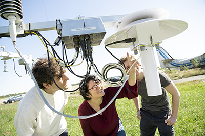 An Ohio State research and two students look at a piece of equipment used to gather data.