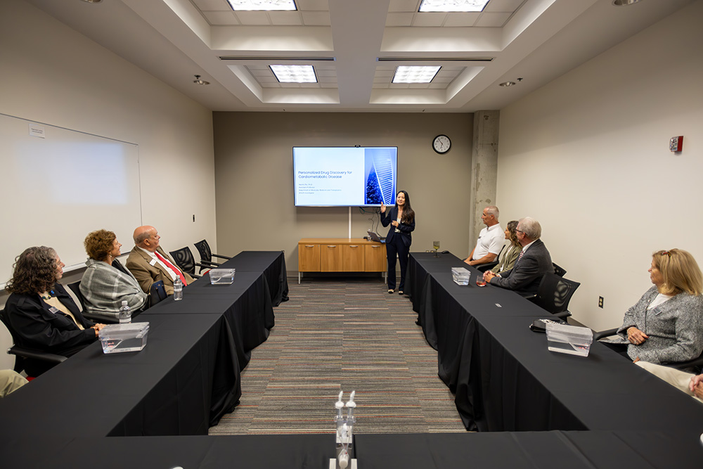 Woman giving a presentation in front of ten other people around a u-shaped table.