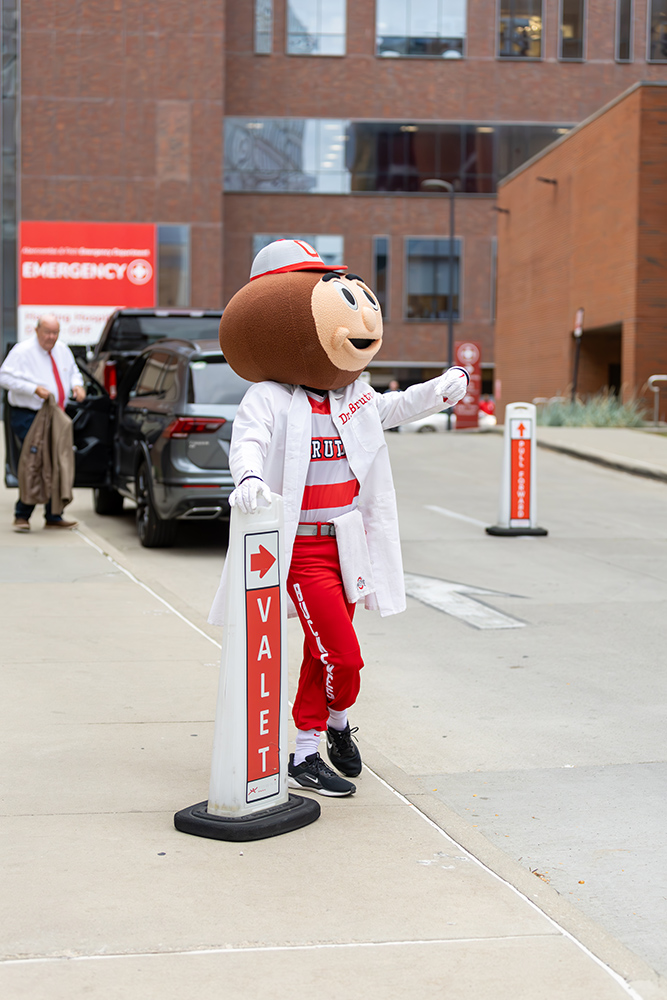 Brutus Buckeye in a lab coat standing by a valet sign