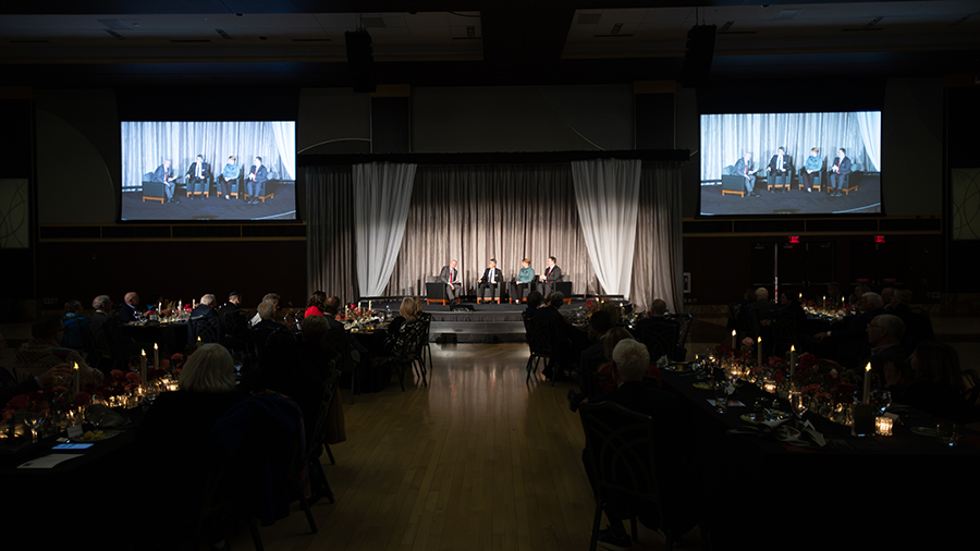 Dr. Wu with other panel members on stage with two screens on each side.