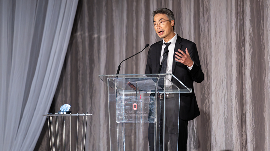 Dr. Wu accepting award standing behind a glass podium.