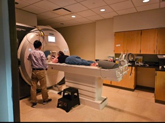 A person lies on a table being prepared for an MRI scan while a technician stands nearby in a medical imaging room.
