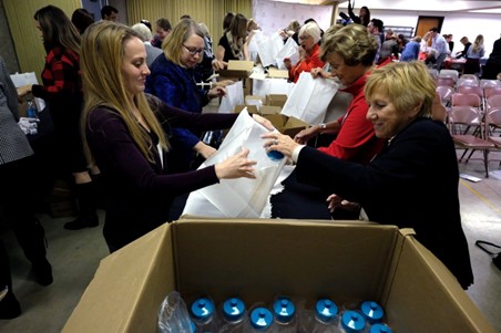 People working together at tables to pack items into bags, with boxes of bottled water in the foreground.