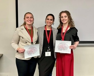 Three people standing together indoors, each wearing a red lanyard, with two of them holding certificates.