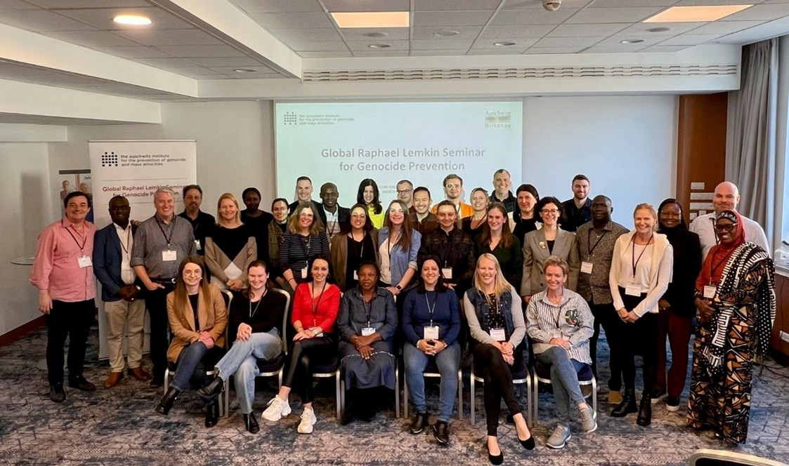 Group photo of participants at the Global Raphael Lemkin Seminar for Genocide Prevention, posed in a conference room with a presentation screen behind them.