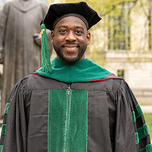 Photo of Evans Osuji, an Ohio State graduate, standing in a cap and gown and smiling