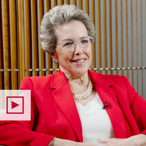 Gifford Weary sits and smiles wearing a red suit jacket, white shirt and pearl necklace.