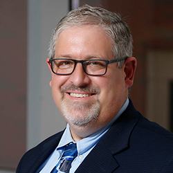 Photo of Dr. Joel Mayerson wearing a dark blue suit and glasses