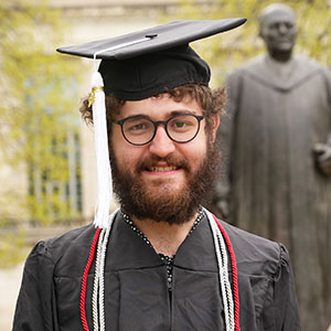 Photo of Nigel Becker, an Ohio State graduate, standing in a cap and gown and smiling