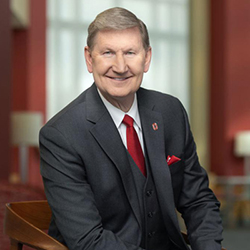 Photo of President Carter, The Ohio State University, as he sits and smiles wearing a dark gray suit, white shirt and scarlet tie