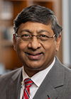 Ravi V. Bellamkonda, a man wearing a gray suit, red tie and glasses is smiling.