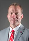 Photo of Ross Bjork, a man wearing a gray suit, white shirt and red tie