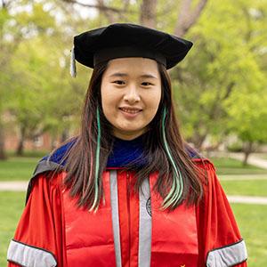 Photo of Shiqi Zhang, an Ohio State graduate, standing in a cap and gown and smiling