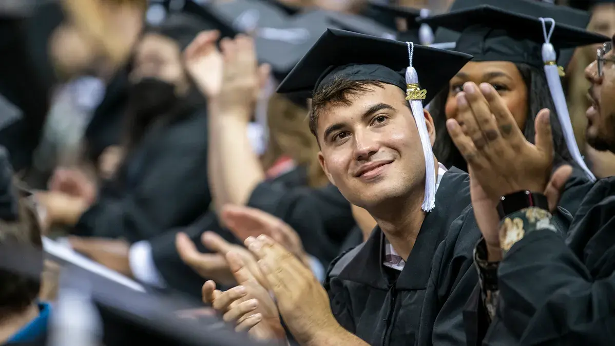 students in caps and gowns clapping during graduation ceremony