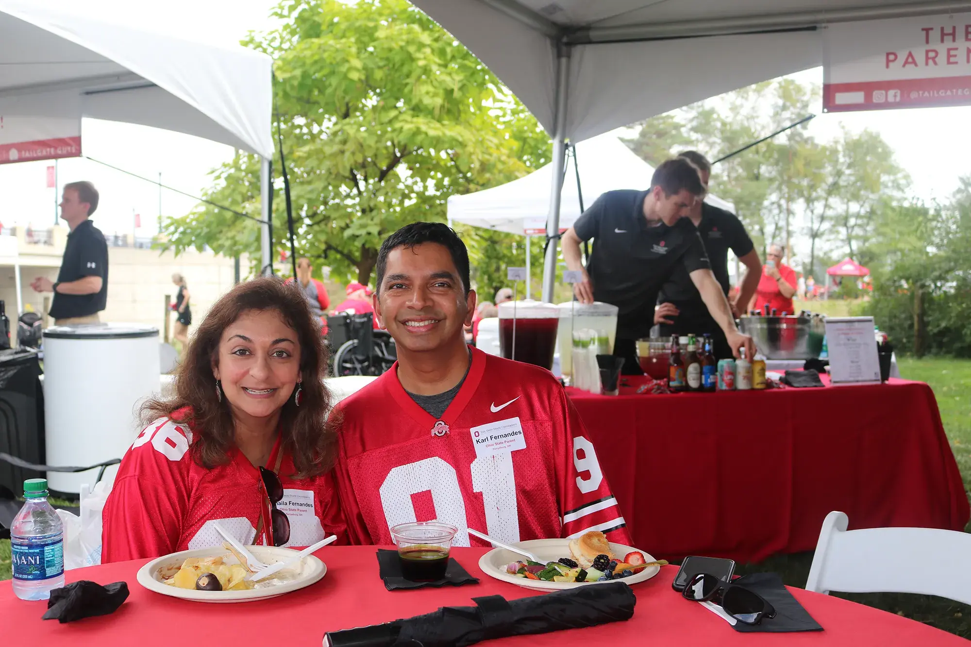 Man and woman wearing ohio state jerseys enjoy a meal under a tent at a Football Tailgate