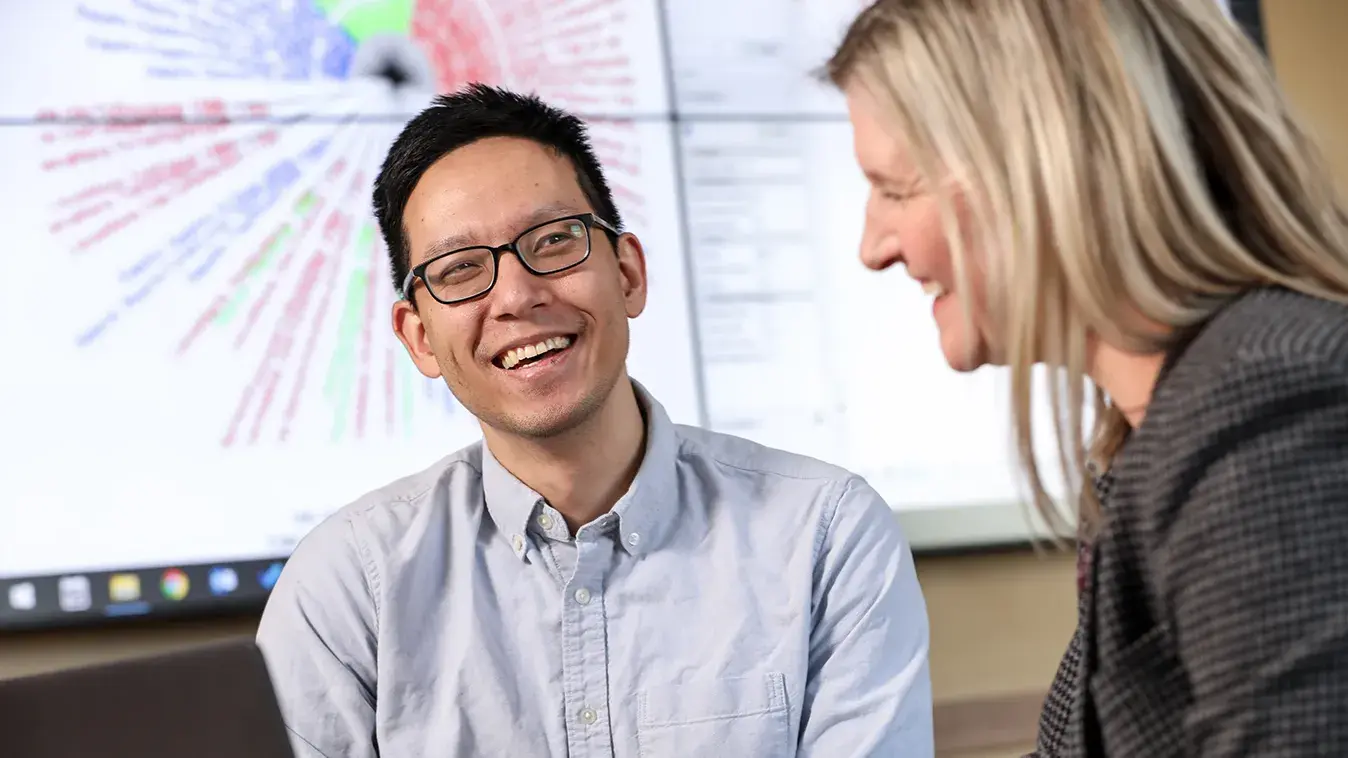 student and professor discussing data in front of a projector smiling