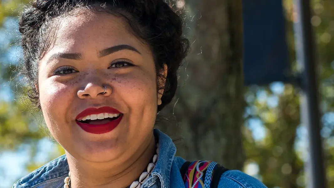 student wearing bright red lipstick and a denim jacket smiling while posing for a picture