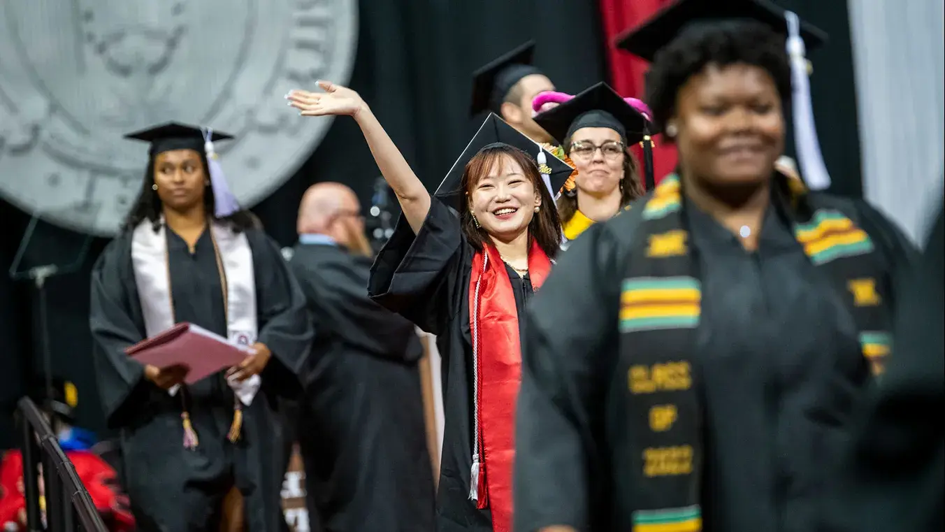 students wave to the crowd while walking at graduation