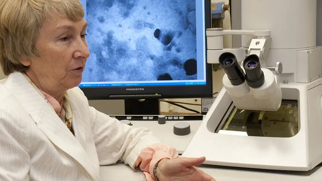 two women talking in front of a monitor showing microscopic views