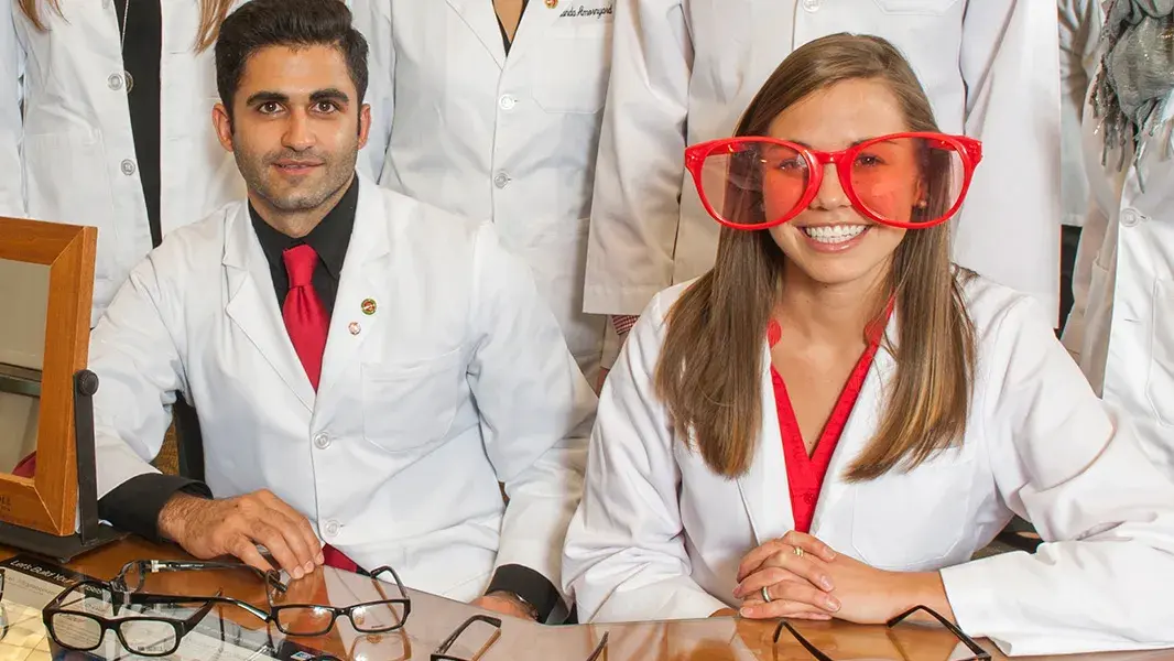 optometry students in white coats wearing oversized funny red glasses