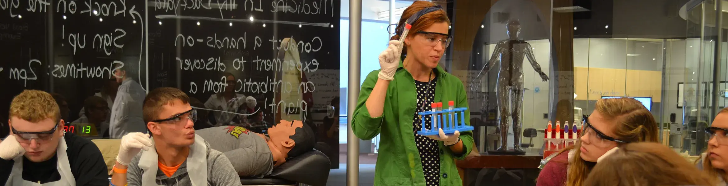 student wearing green jacket holding test tubes in her hands