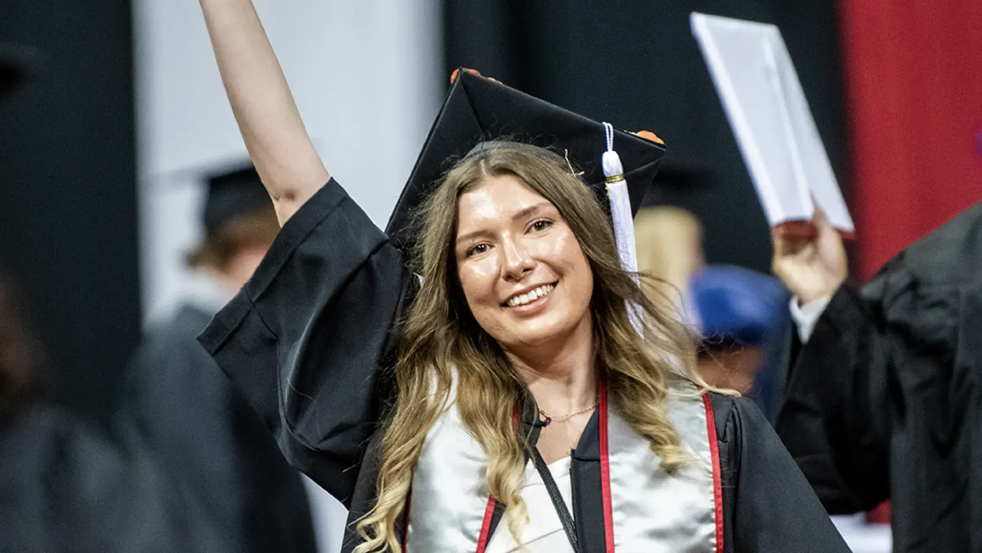 woman in cap and gown waving to the audience after receiving her diploma