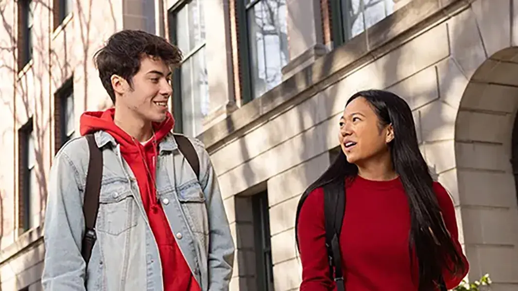 two students wearing warm jackets walking across campus in the fall