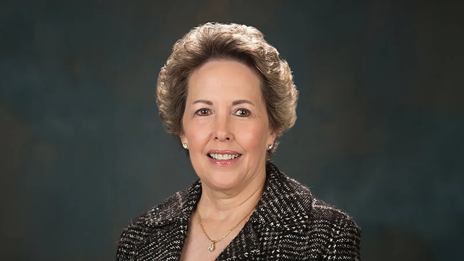 Gifford Weary wearing a dark jacket and necklace posing for a portrait