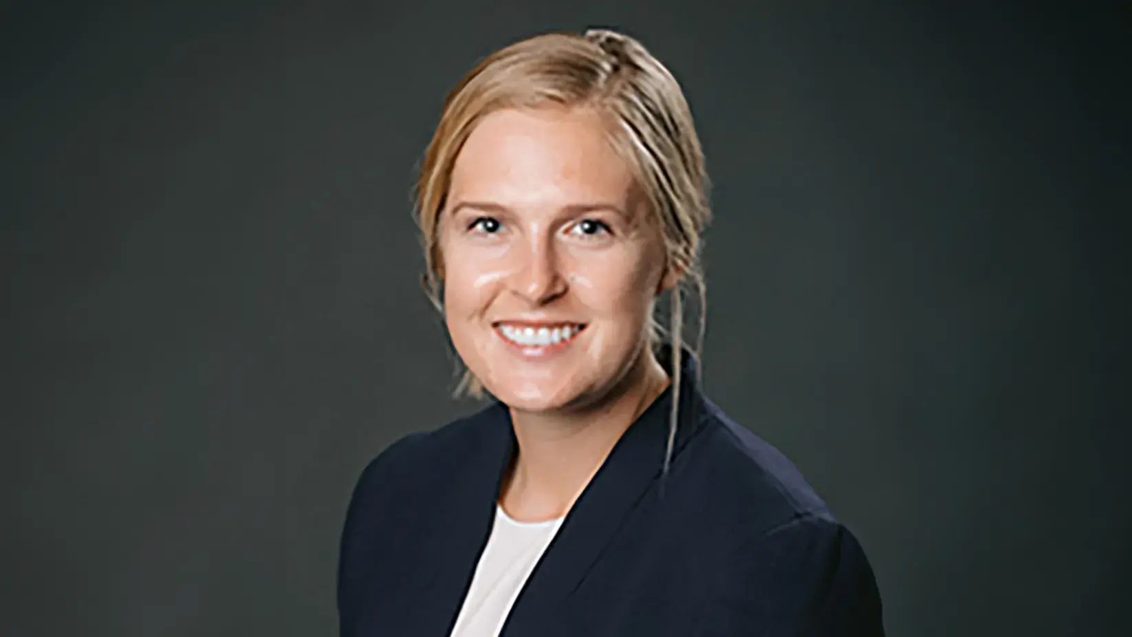 Caitlyn Skavdahl in a suit posing in front of a gray backdrdop