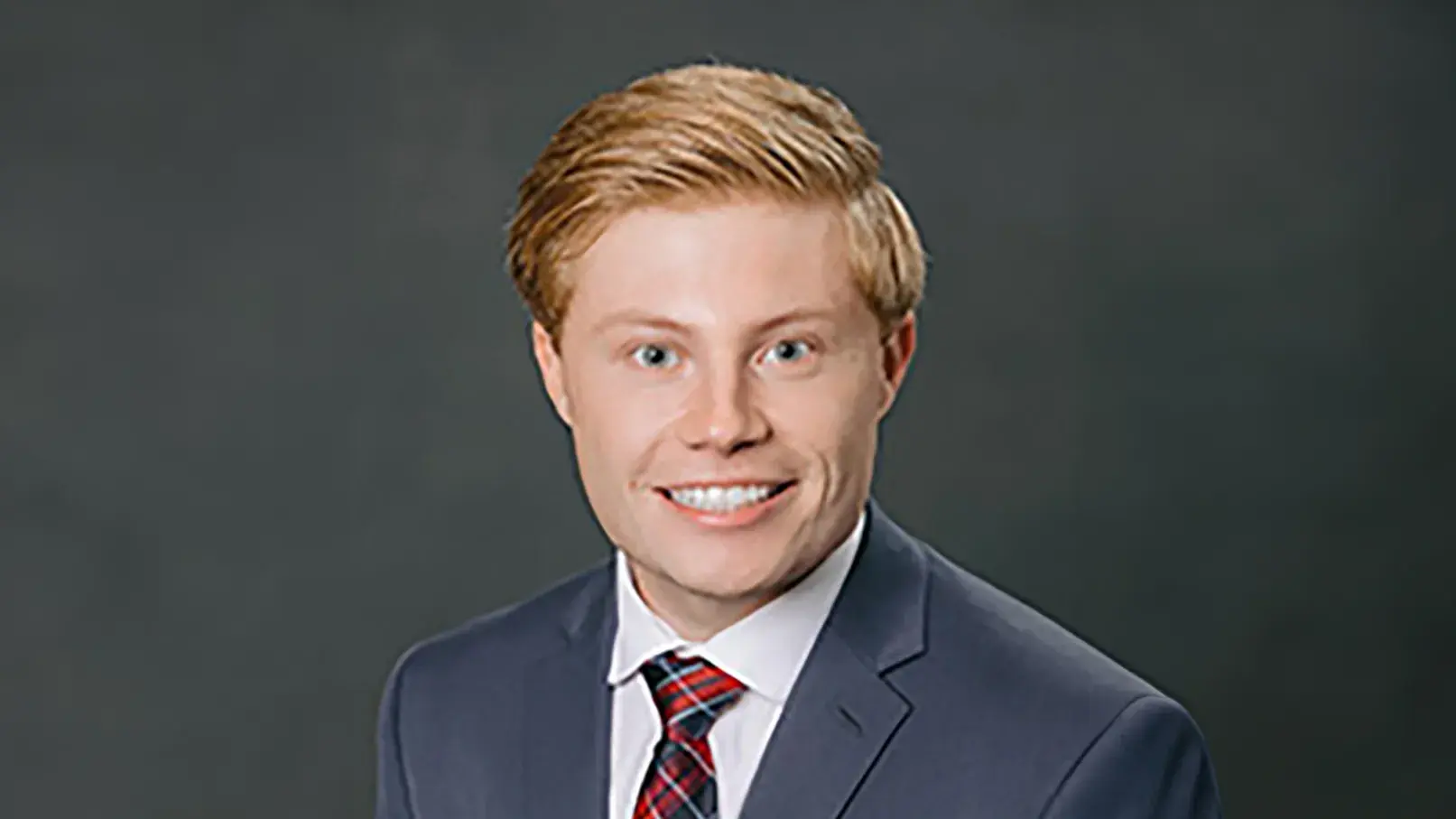 Cooper Karras in a suit posing in front of a gray backdrdop