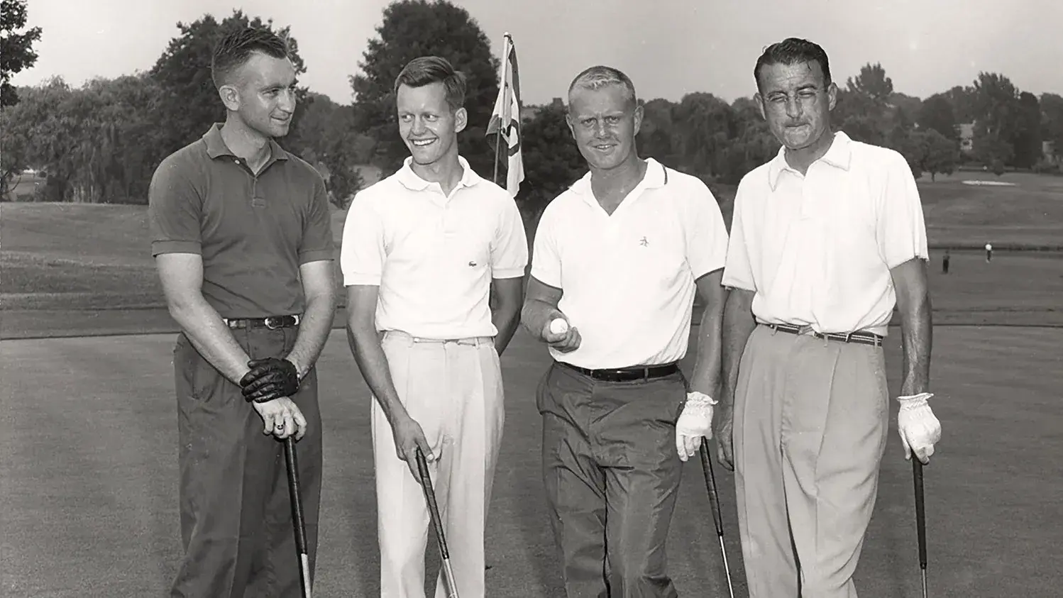 black and white photo of four men holding golf clubs posing for a photo
