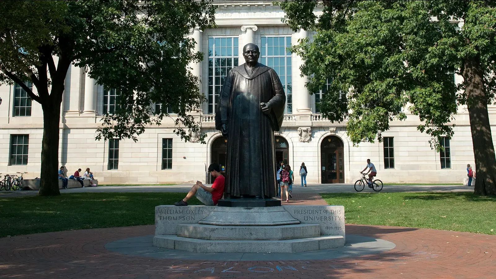 student leans on a statue in front of a white brick building on osu's campus