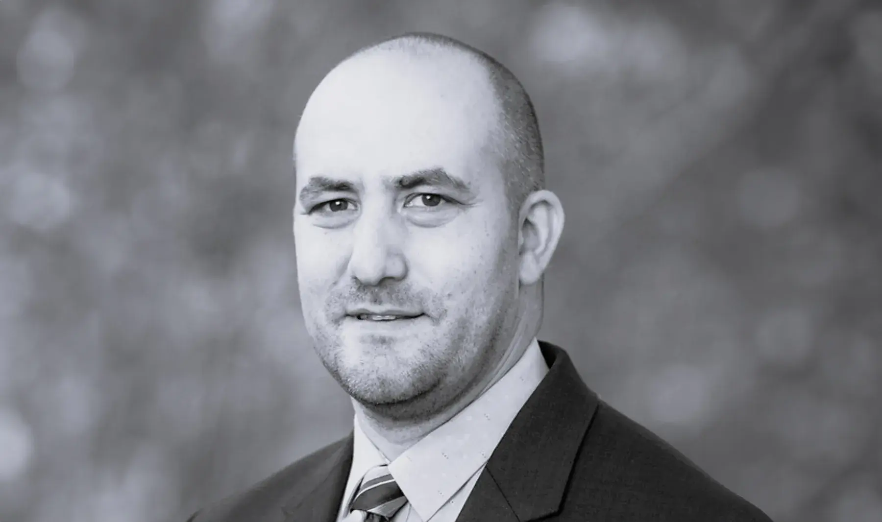 black and white portrait of Micah Berman, JD outdoors wearing a dark suit and tie