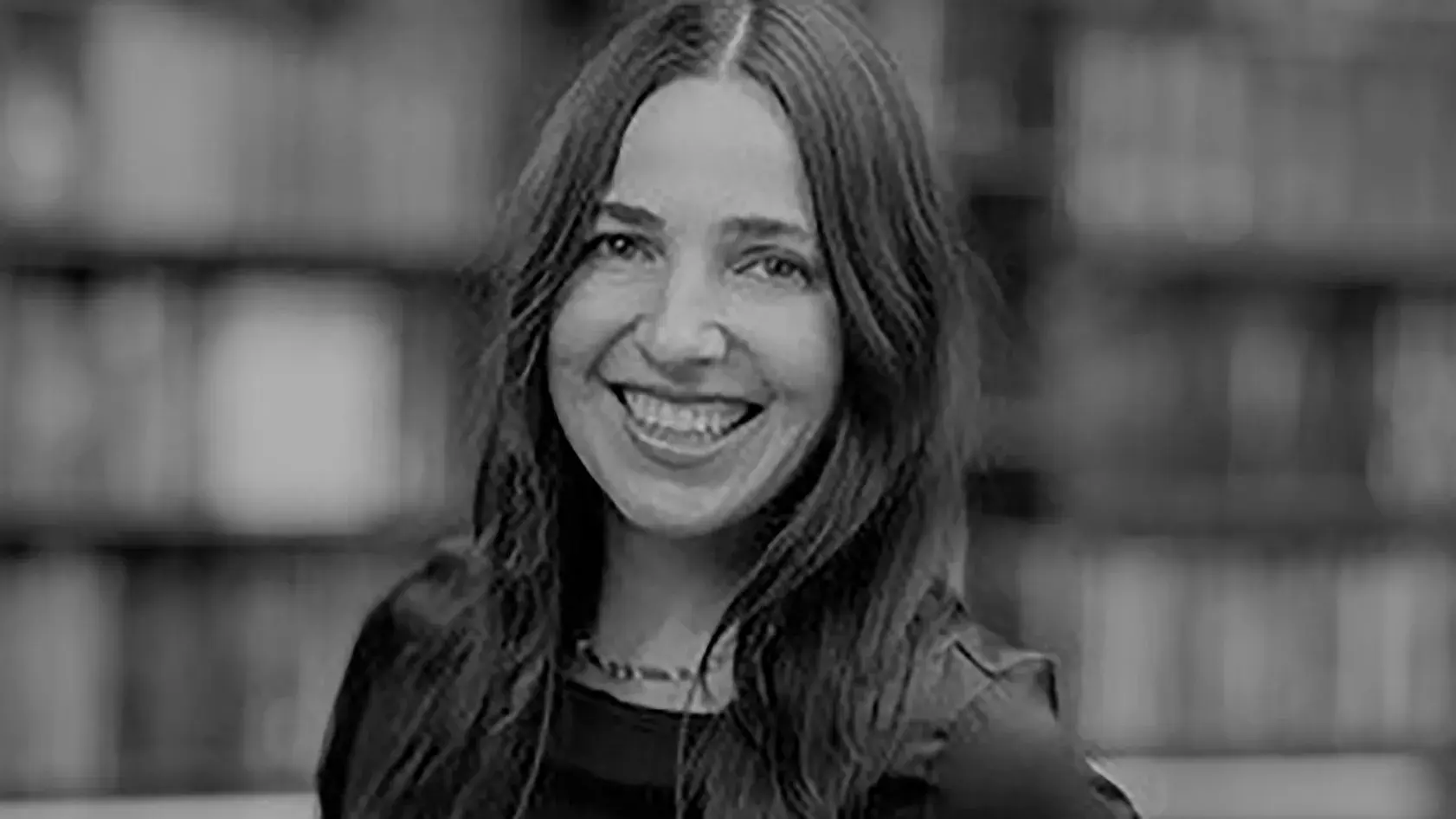 black and white portrait of Mara Frazier smiling in front of a shelves of books