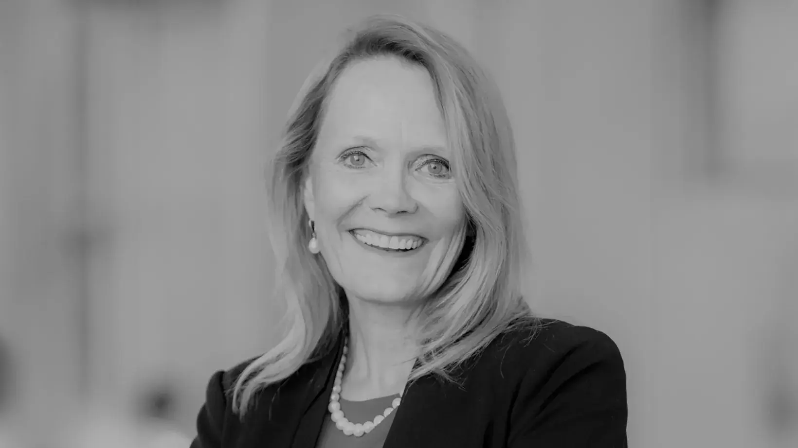 black and white portrait of Sharon Tucker, PhD smiling, wearing a dark suit coat and pearl necklace