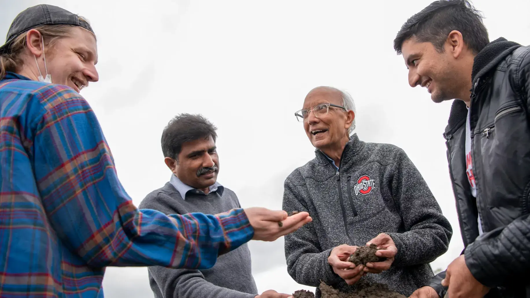 four men laughing outside while examining soil samples