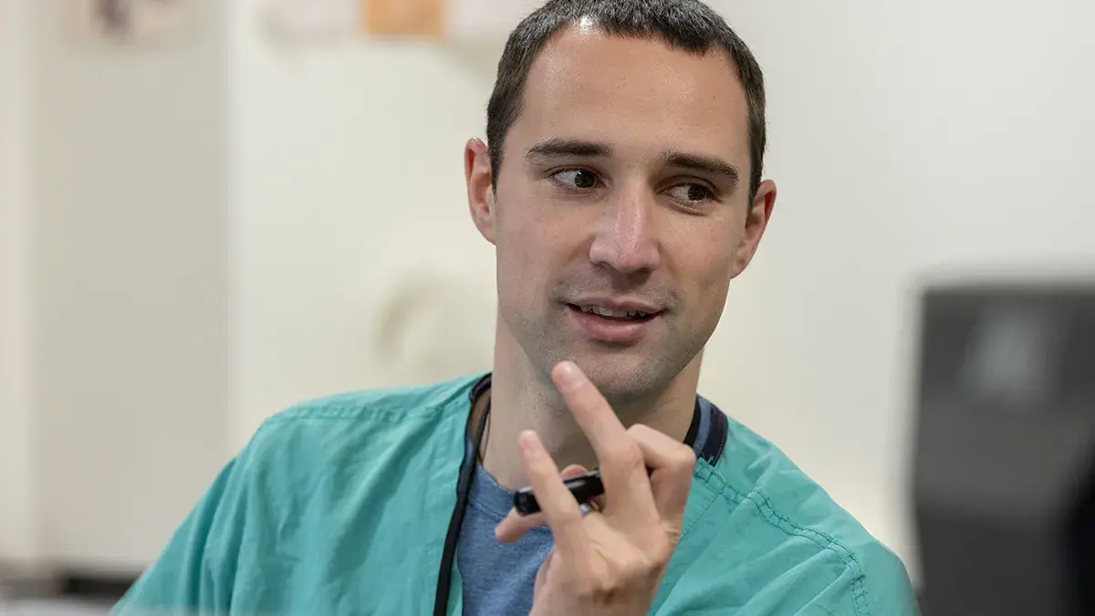 Aaron Craft is talking to someone while holding a pen and wearing scrubs
