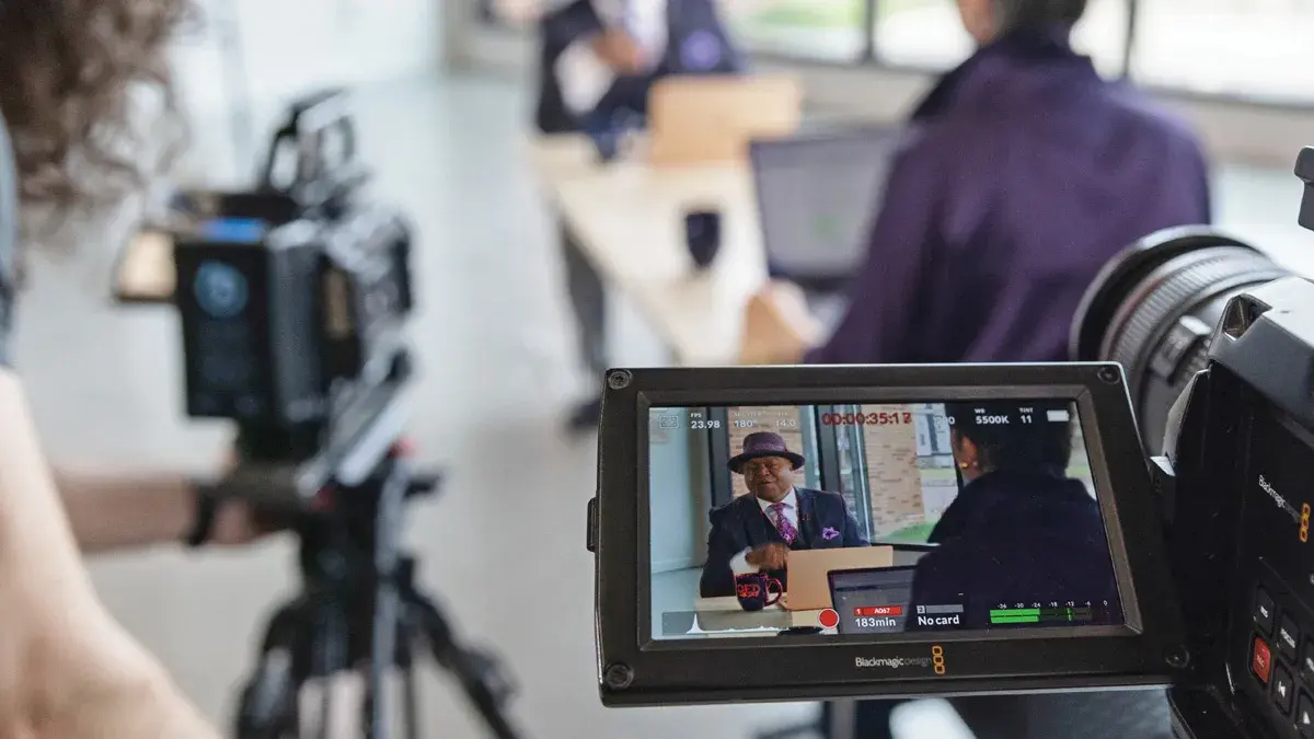Picture of an interview taking place between a man in a hat and a woman with her back to the camera