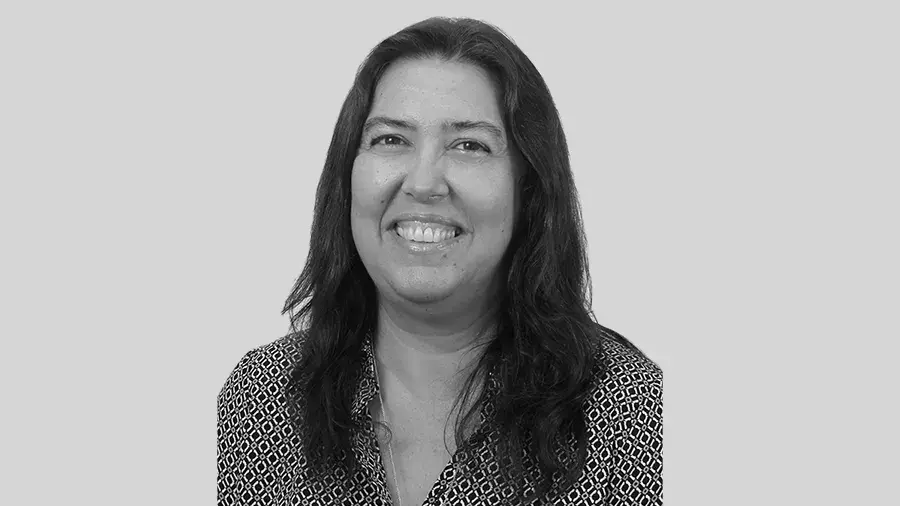A woman with long, brown hair and wearing a black and white shirt poses and smiles for the camera