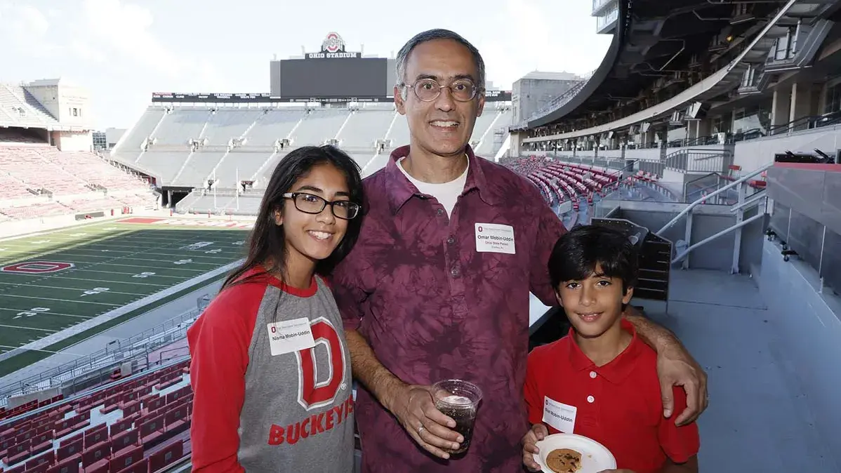 A dad, daughter and son stand and smile in Ohio Stadium at the Buckeye Family Picnic