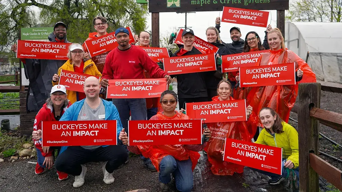 A group of people pose for a volunteer picture holding signs that say, "Buckeyes make an impact"