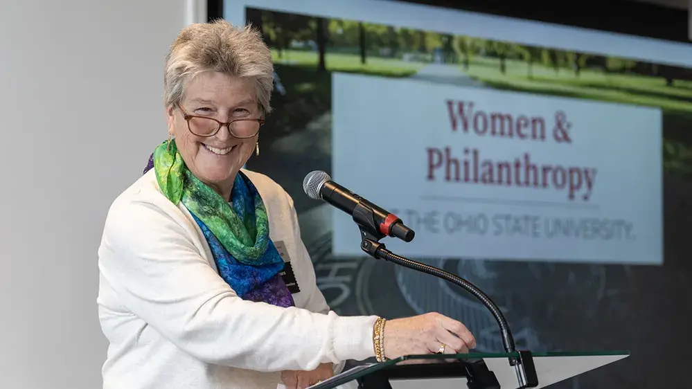 A woman stands at a podium and takes a moment to smile for the camera during her speech