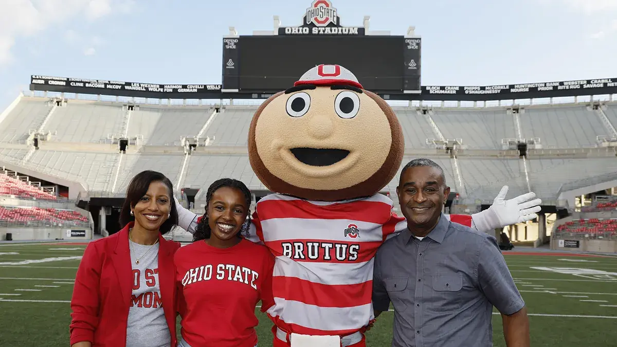 A mother, daughter and father stand with Brutus Buckeye in Ohio Stadium.