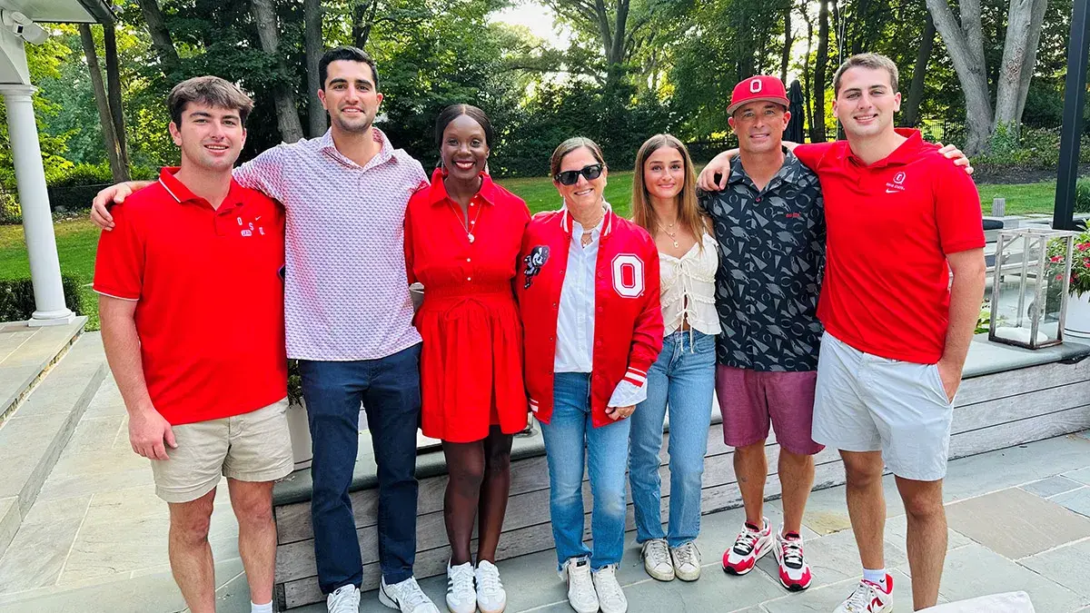 A group of seven people all dressed in scarlet and gray clothing stand outside on a patio.