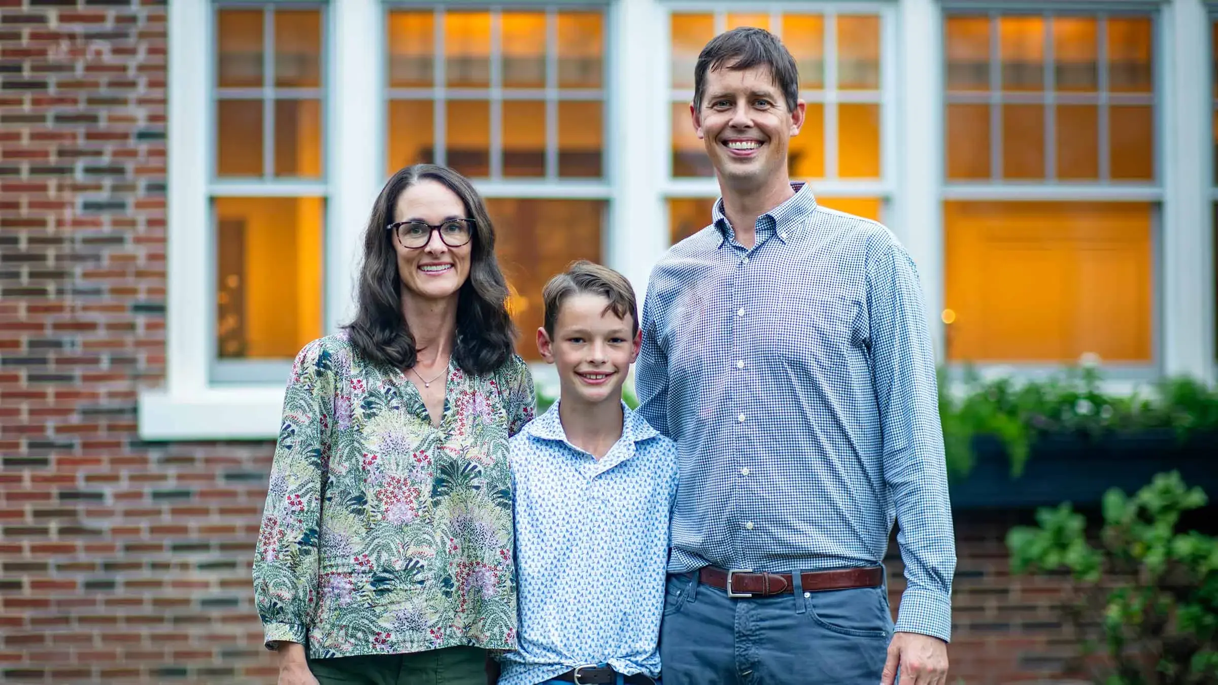 Family of three posing for a portrait photo outside a brick home.