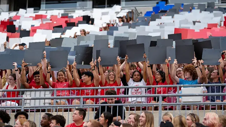 Students in a crowd holding up different colored signs.